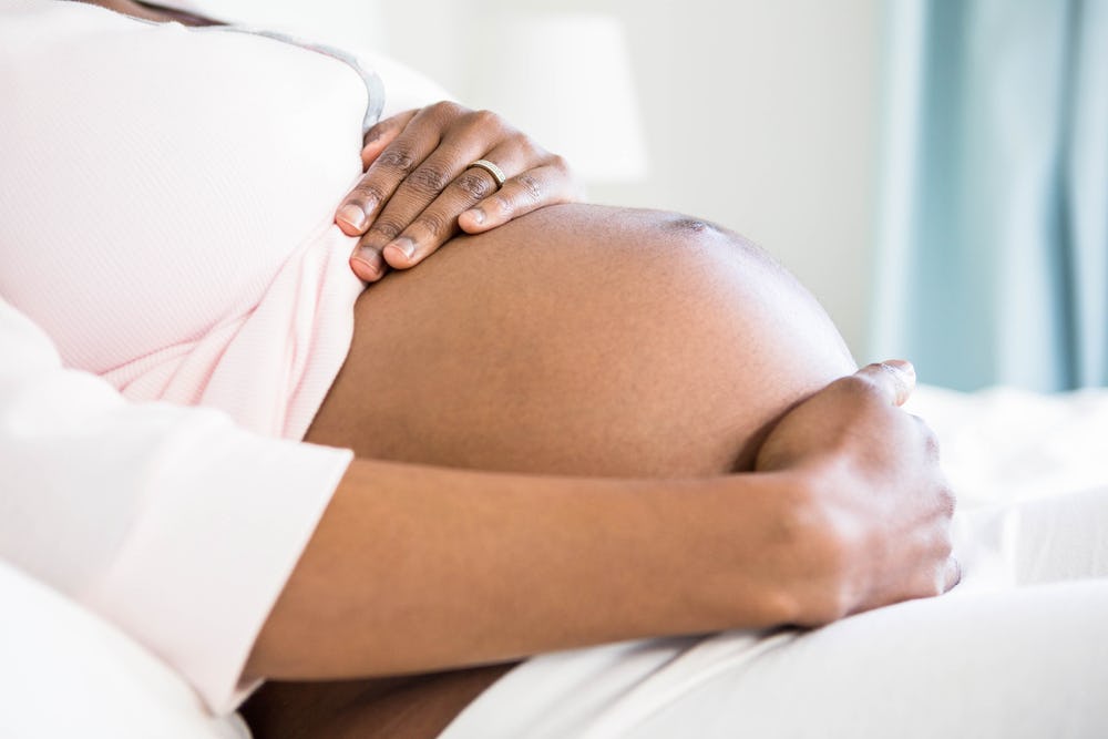 A woman dealing with perinatal depression holding her pregnant belly while lying in a hospital bed