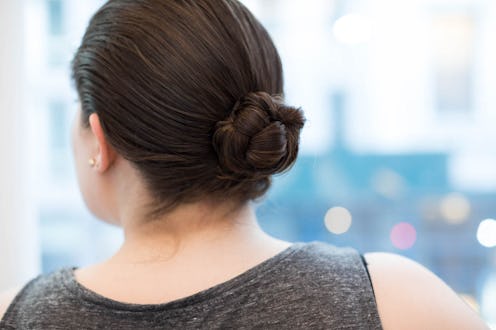 The back of a brunette woman in a grey top with her hair up in a bun