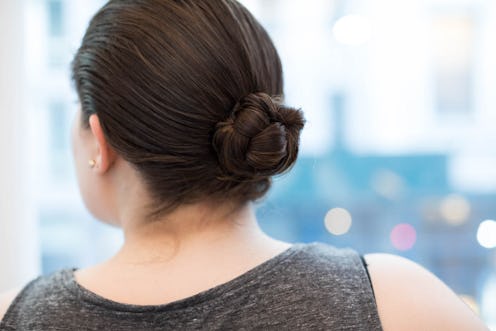 The back of a brunette woman in a grey top with her hair up in a bun