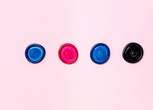  Four condoms in blue, red and black on a pink backdrop.