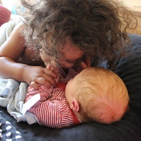 A toddler girl kissing her new born baby brother