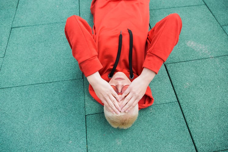 A man laying on the ground, holding his head because of chronic migraine.