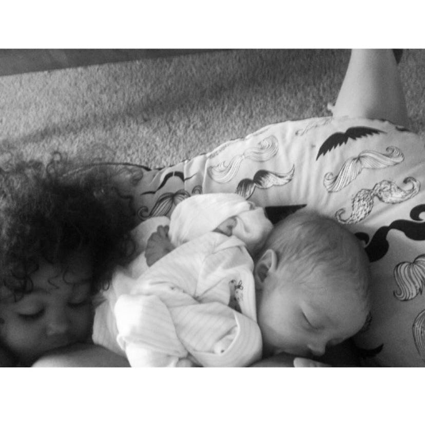 A mother breastfeeding her toddler daughter and her newborn baby at the same time while lying on the...