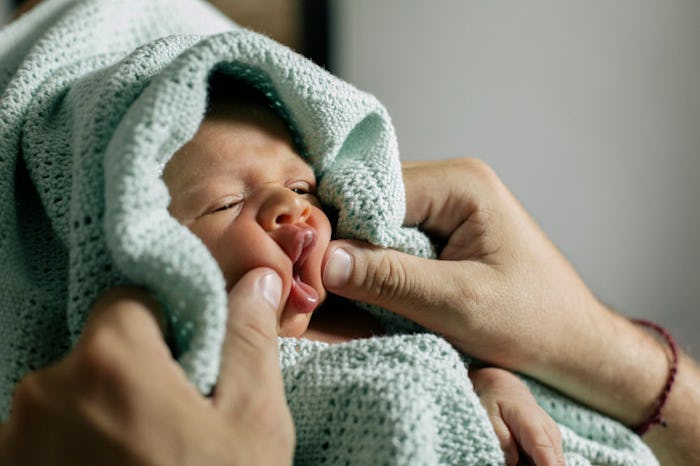 A mother holding a baby wrapped in a blue blanket and playing with its face