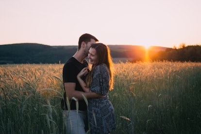 A happy couple embraces in a field at sunset.