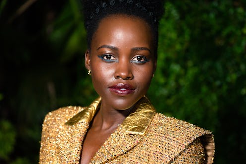Lupita Nyong'o posing in a gold jacket at a pre-oscars dinner