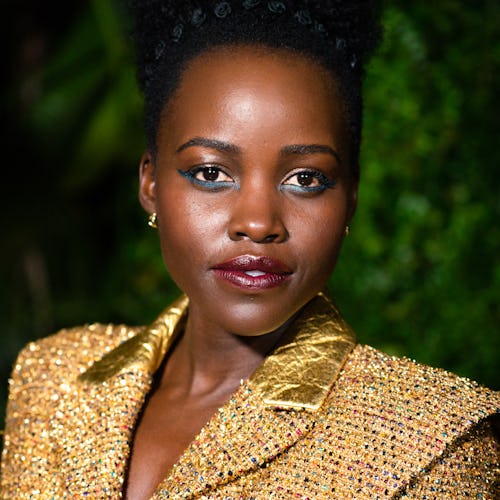 Lupita Nyong'o posing in a gold jacket at a pre-oscars dinner