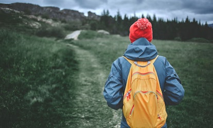 A person wearing an orange cap, a blue jacket, and a yellow backpack hiking on a mountain.