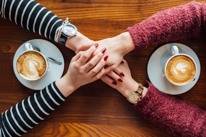 Two women holding hands while having a cup of coffee