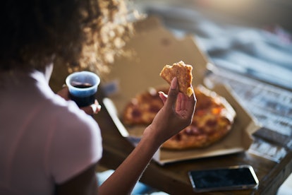 A person is eating pizza, while holding soda in their other hand. Pizza is a classic comfort food fo...