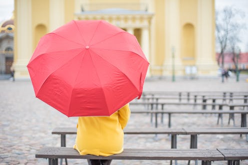 A person wearing a yellow raincoat and a red umbrella in front of a Cathedral