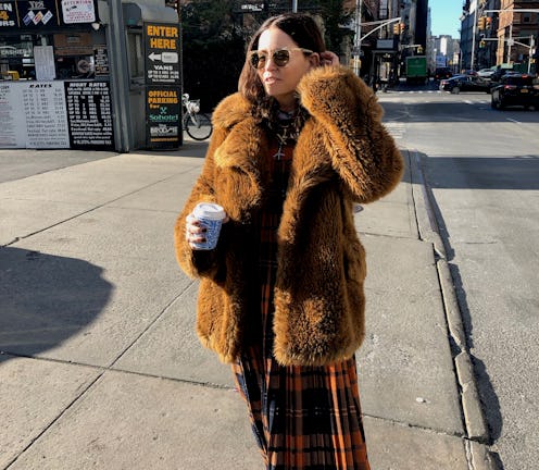 Karin Bereson in a faux fur coat, a long plaid skirt and sunglasses, holding a to-go coffee cup