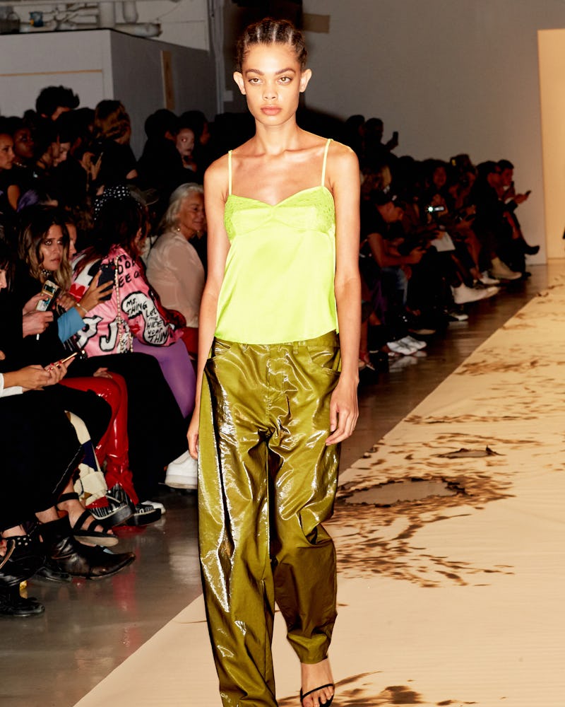 A female model walking in a yellow shirt and slime green pants
