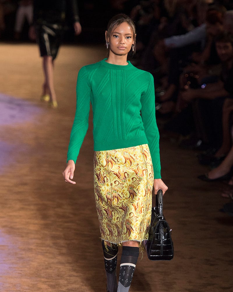 A model walking in a green shirt and yellow skirt 