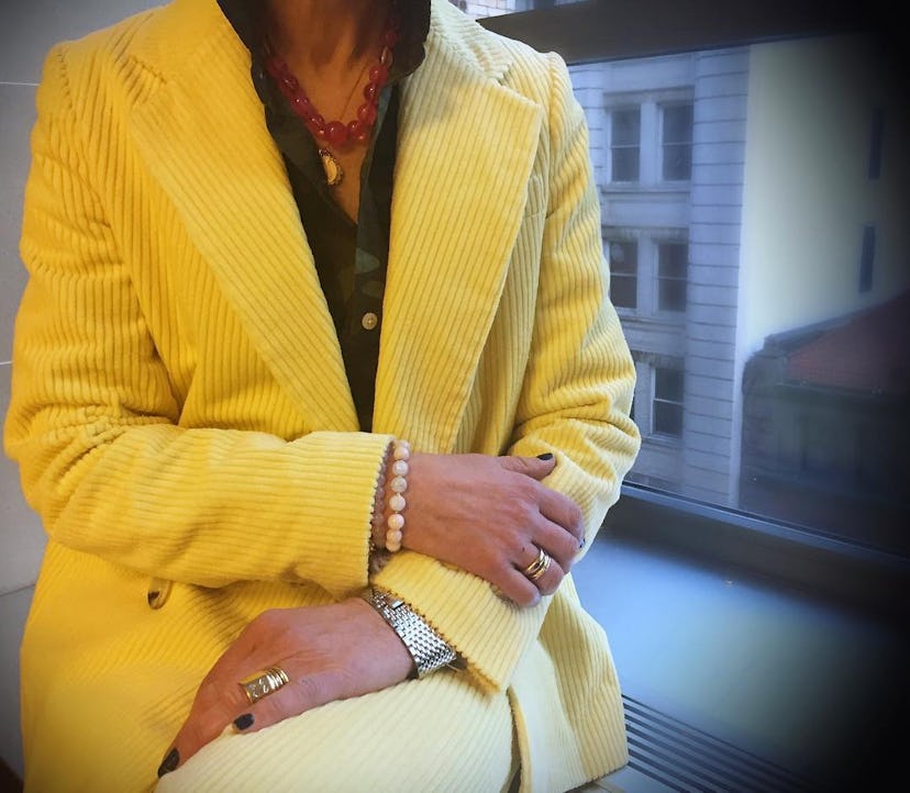 Jacqui Getz sitting next to a window in a yellow velvet suit.