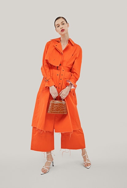 A woman in an orange dress posing with a brown bag