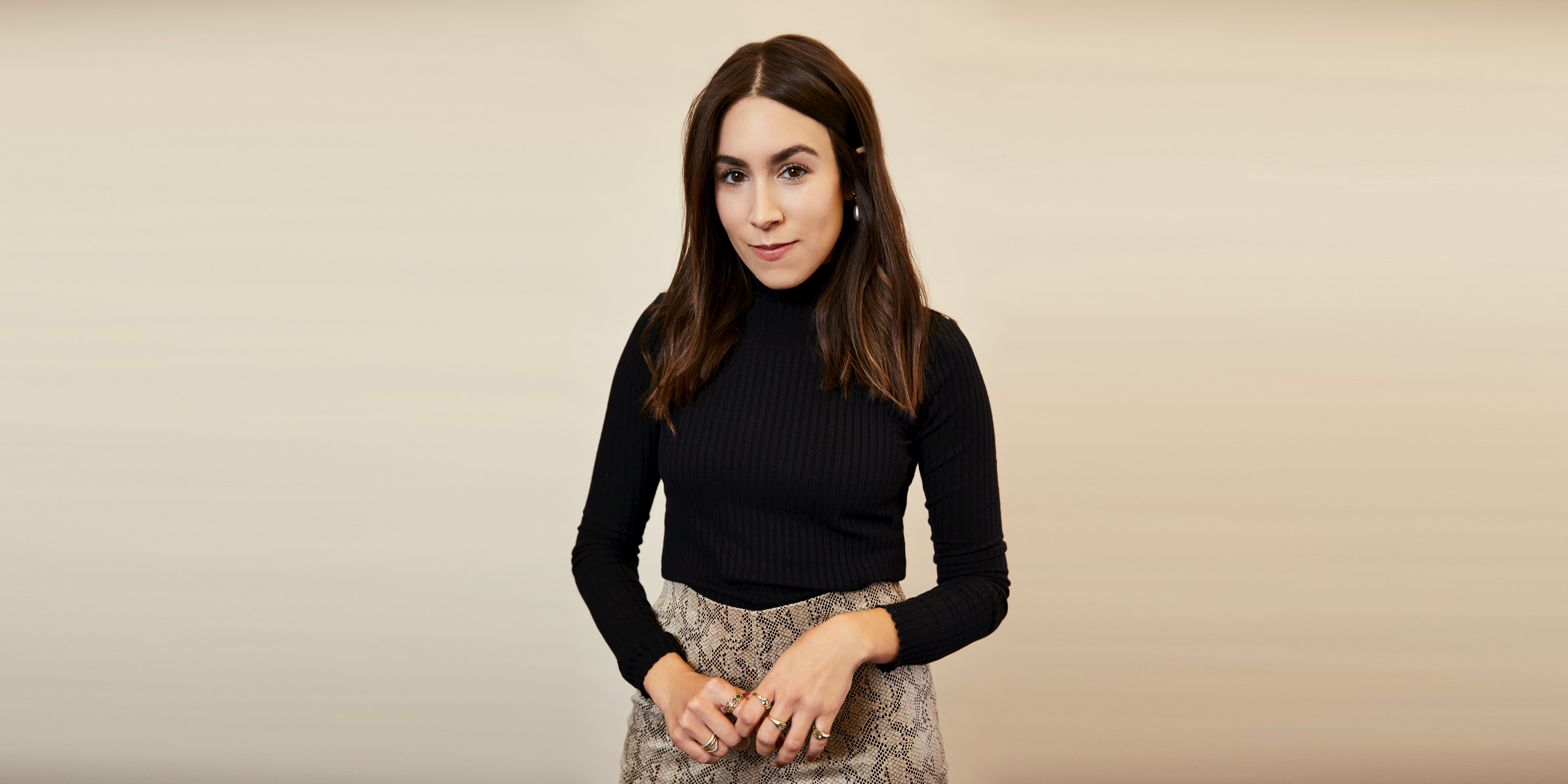 Lauren Caruso posing in a black turtleneck and beige skirt