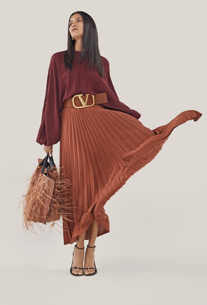 A model posing in a maroon top, with a brown skirt, matching belt and handbag