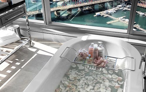 A bathtub filled with white petals in a bathroom with large windows and a view of a big city