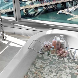 A bathtub filled with white petals in a bathroom with large windows and a view of a big city