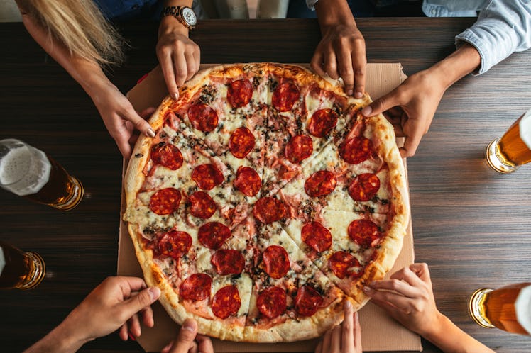 A group of people's hands digs into a pepperoni pizza.