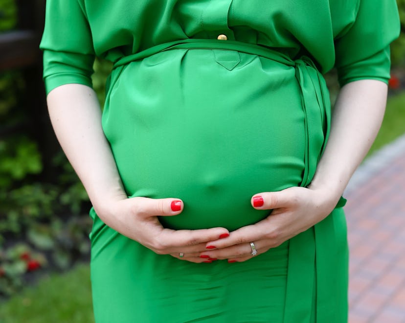 pregnant woman wearing a green dress, holding her bump