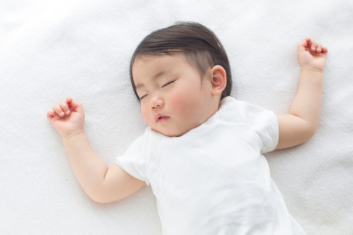 A congested baby lying on its back on a white bed sleeping