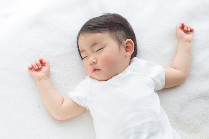 A congested baby lying on its back on a white bed sleeping 