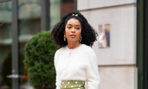 Yara Shahidi standing outside in a white sweater and a green polka dot pants with a small pink bow i...