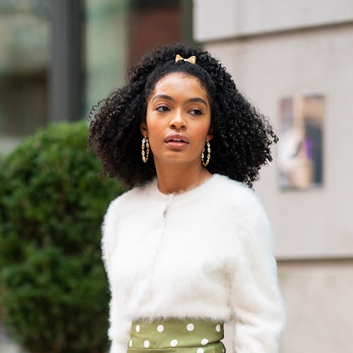 Yara Shahidi standing outside in a white sweater and a green polka dot pants with a small pink bow i...