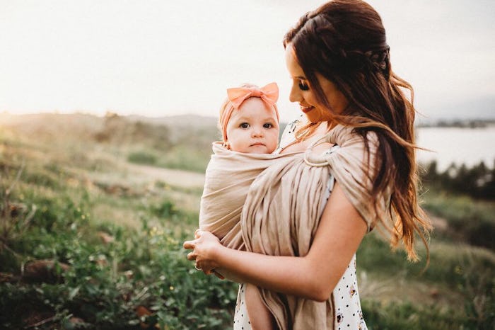 A mother holding her baby with a baby carrier on her chest