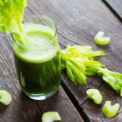 A glass of celery juice garnished with a fresh celery on a wooden table