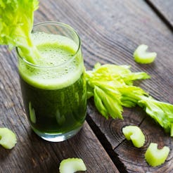 A glass of celery juice garnished with a fresh celery on a wooden table