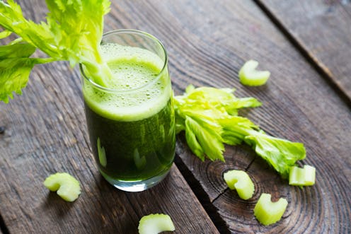 A glass of celery juice garnished with a fresh celery on a wooden table