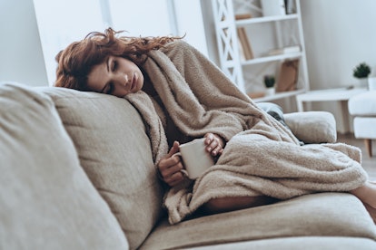 A woman leaning on her couch covered with a blanket and drinking tea with a weakened immune system
