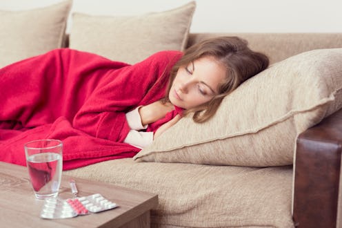A woman lying on her bed covered with a blanket and meds in front of her for her weakened immune sys...