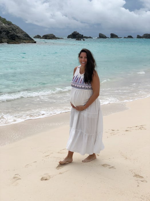 A pregnant woman wearing a white summer dress on a sand beach