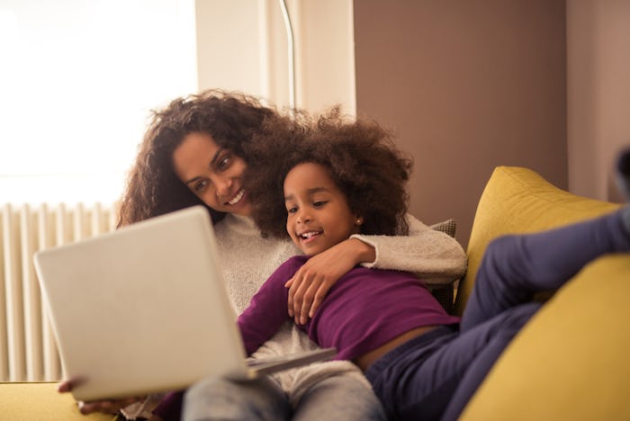 A mom on the computer, holding her daughter and laughing.