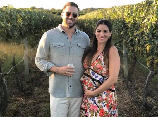 Alyssa Himmel holding her pregnant belly while posing next to her husband in a vineyard