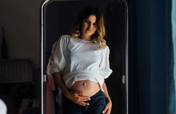 Pregnant woman examining her pregnant stomach in the mirror
