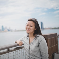 Sabrina Qiao, diagnosed with a chronic autoimmune disease standing next to a river with the NYC in h...