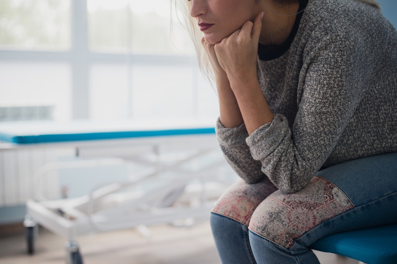 A woman struggling with depression, sitting with elbows on her knees, holding her head with her hand...