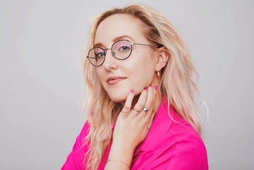 A blonde with glasses, wearing a pink shirt, smiling for a photo