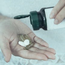 A person putting two white pills into his hand from a pill bottle