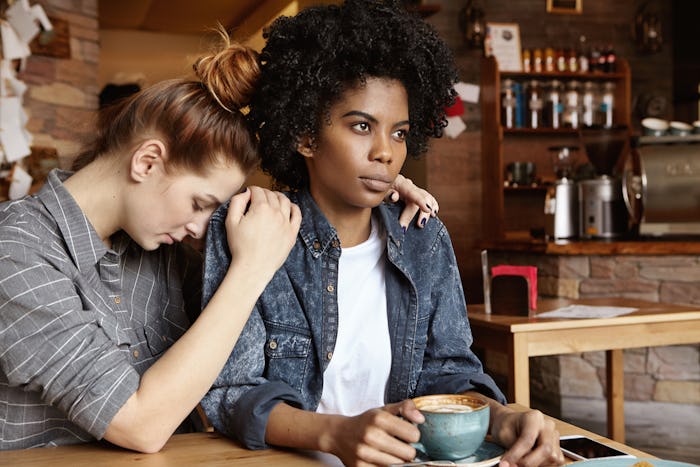 A woman struggling with anxiety resting her head on her friend's shoulder in a coffee shop
