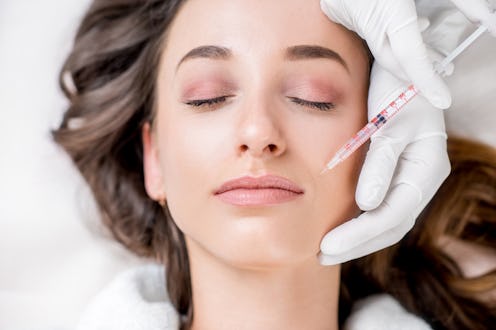 A woman lying down with closed eyes as gloved hands inject filler above her lips