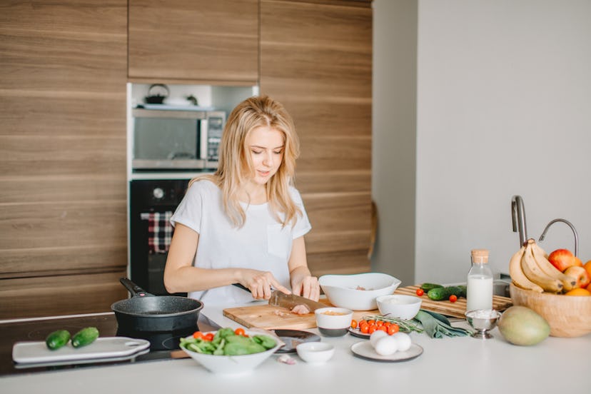 A woman chopping up various healthy fruits and vegetables in the kitchen