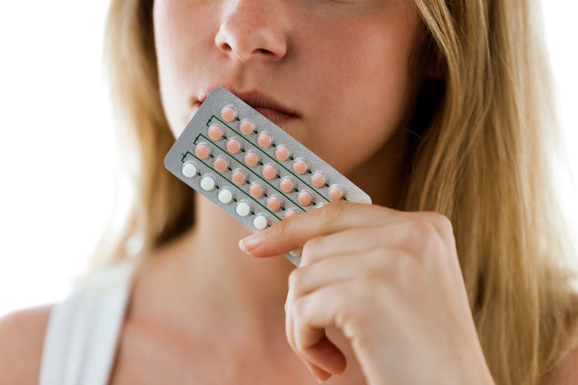 A woman holding a packet of birth control pills to her face