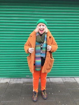 Aoife Hanna wearing an orange faux fur coat, tracksuit, and a green beanie with a colorful scarf whi...
