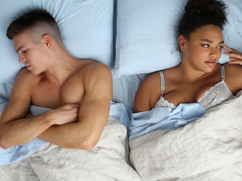 An awake girl in a bed next to her boyfriend that is sleeping